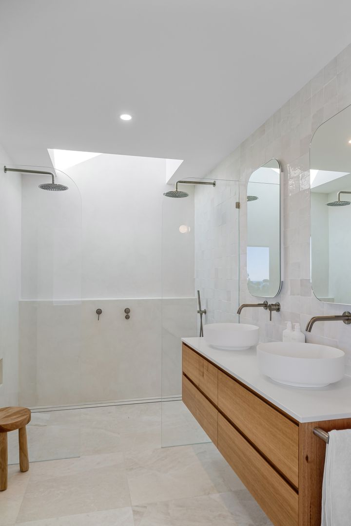 A real bathroom with wood vanity cabinets, paired mirrors, and a glass shower.